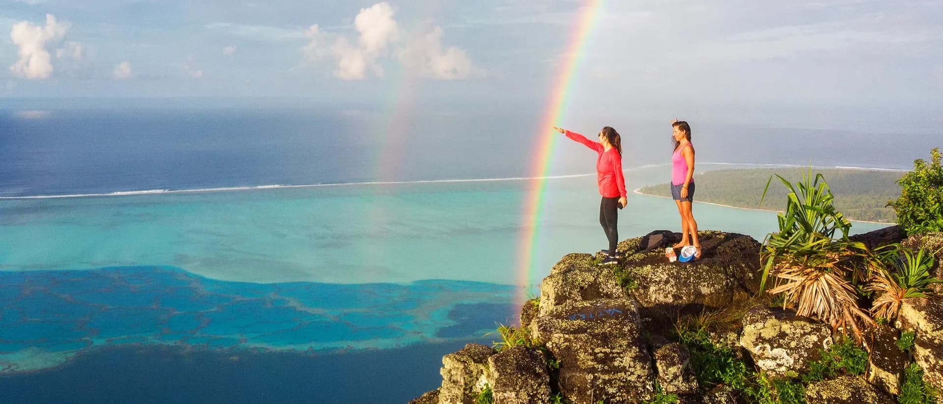Two Sailing Virgins sailors on a clifftop above the lagoon under a rainbow