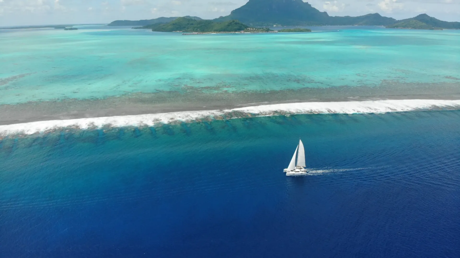 Catamaran sailing along the reef in deep blue water off Bora Bora