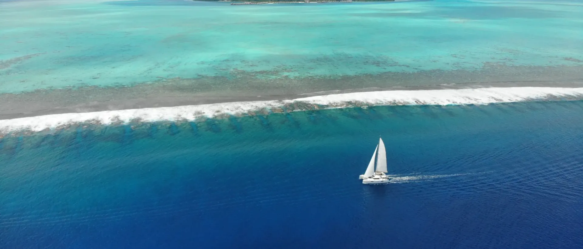 Catamaran sailing along the reef in deep blue water off Bora Bora