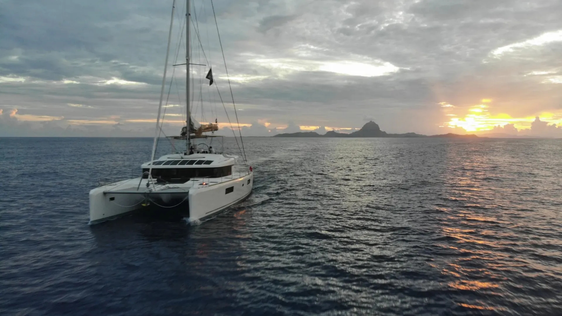 Sailing catamaran at sunset in French Polynesia with Bora Bora on the horizon