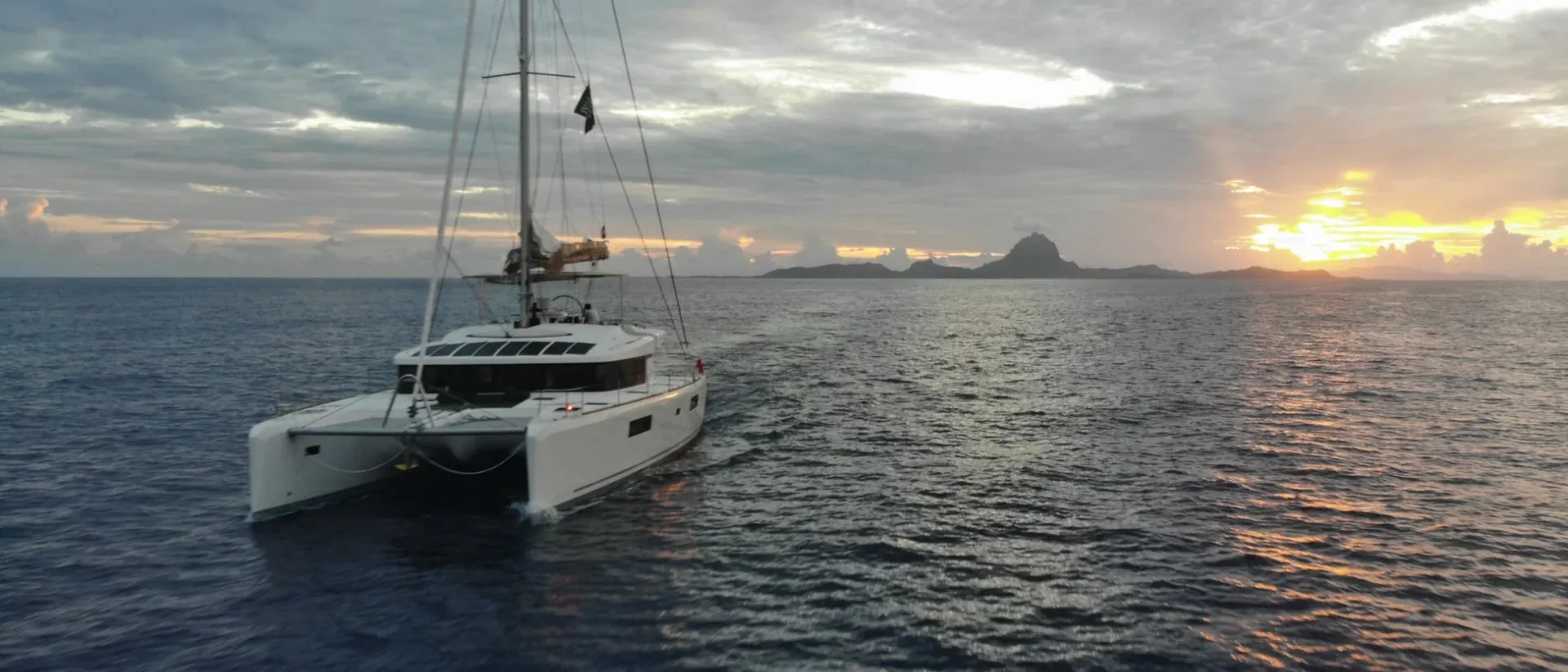 Sailing catamaran at sunset in French Polynesia with Bora Bora on the horizon