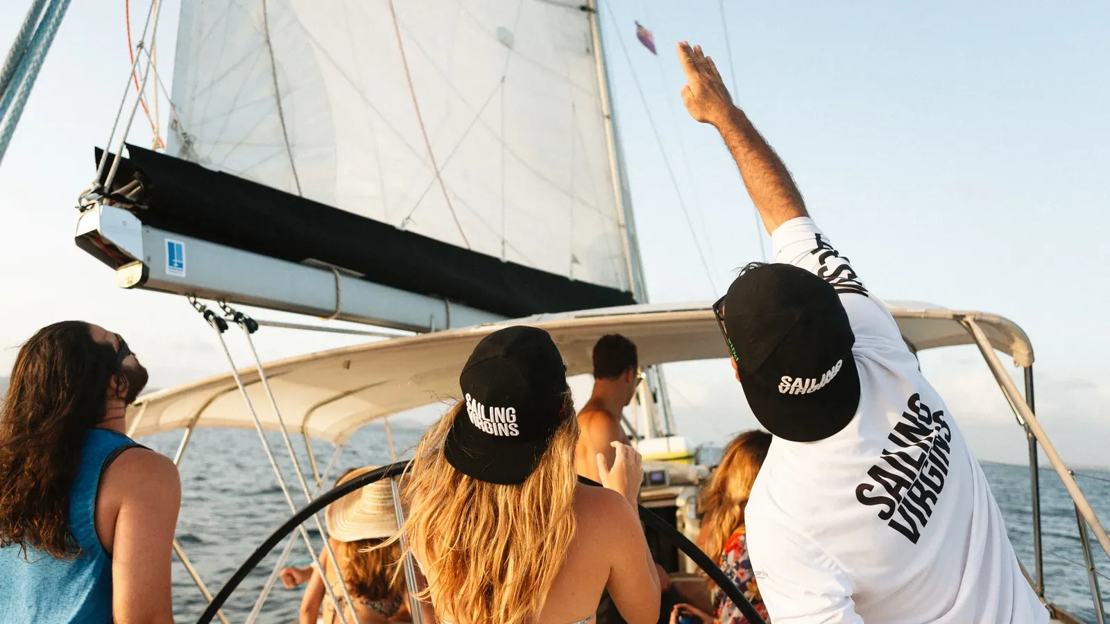 Crew in Sailing Virgins caps trimming the sails at sunset