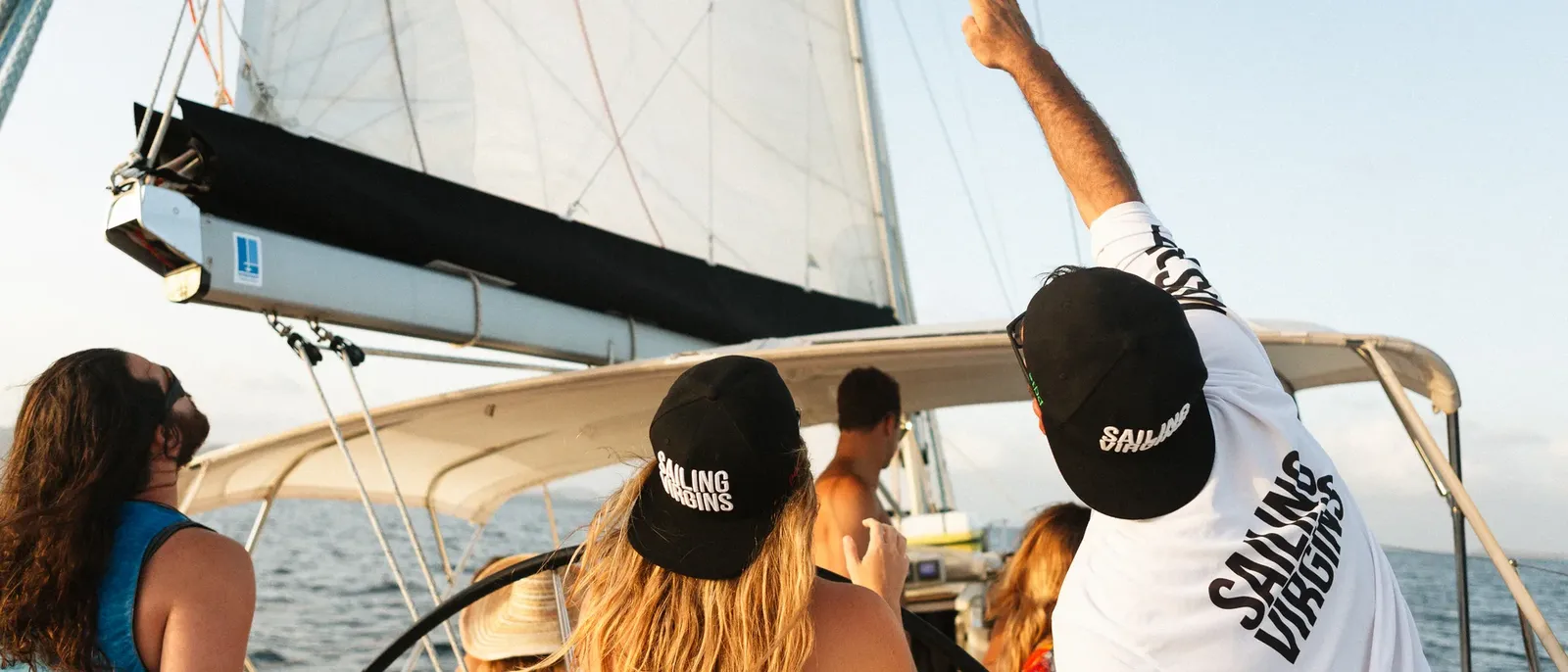 Crew in Sailing Virgins caps trimming the sails at sunset