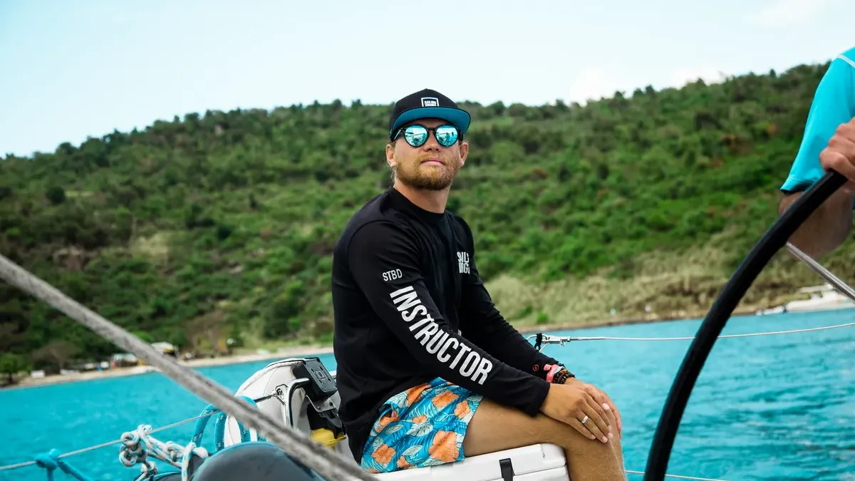 A Sailing Virgins instructor at the helm in a turquoise anchorage